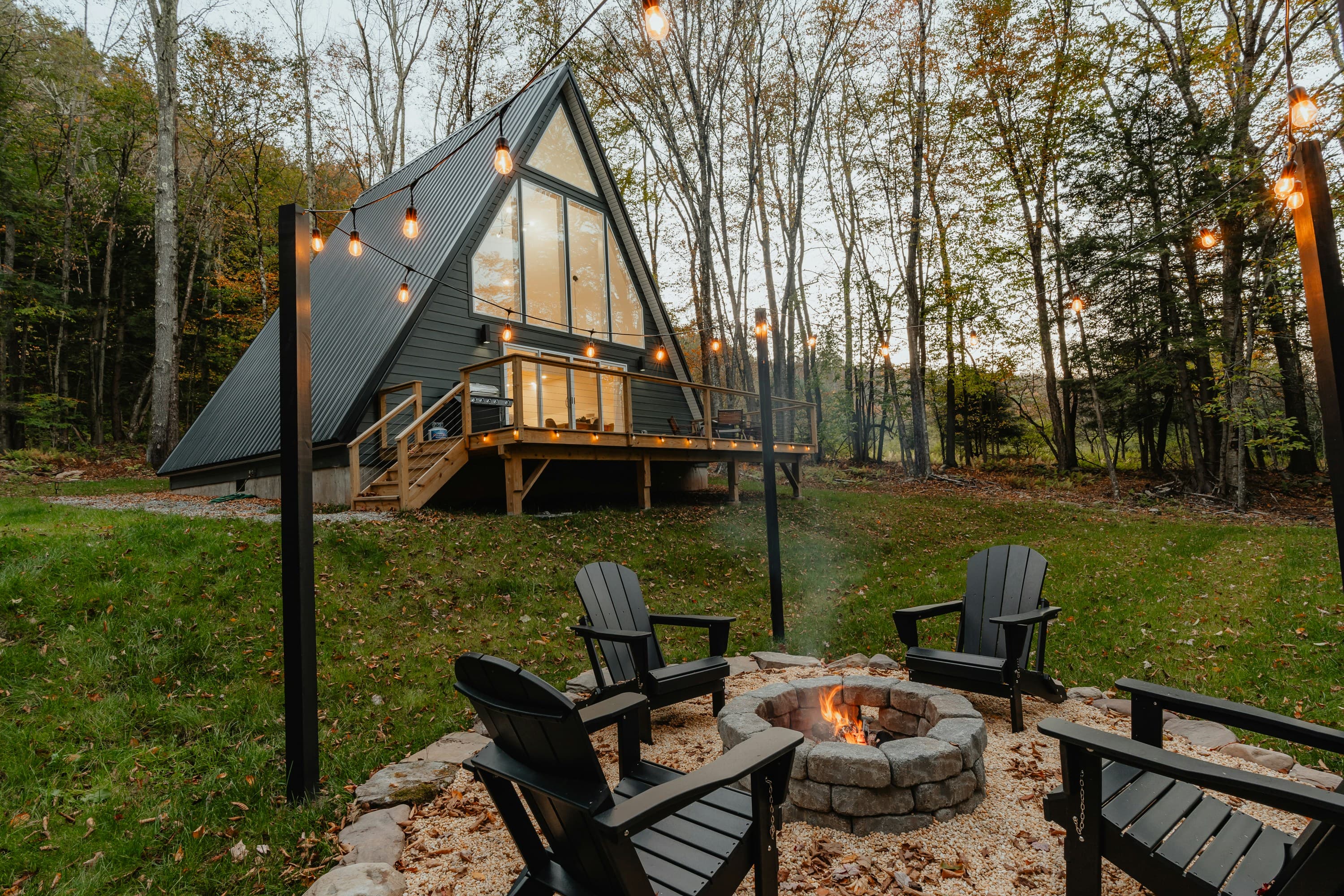 A-frame cabin with a back patio, string lights, and chairs around an outdoor fire pit