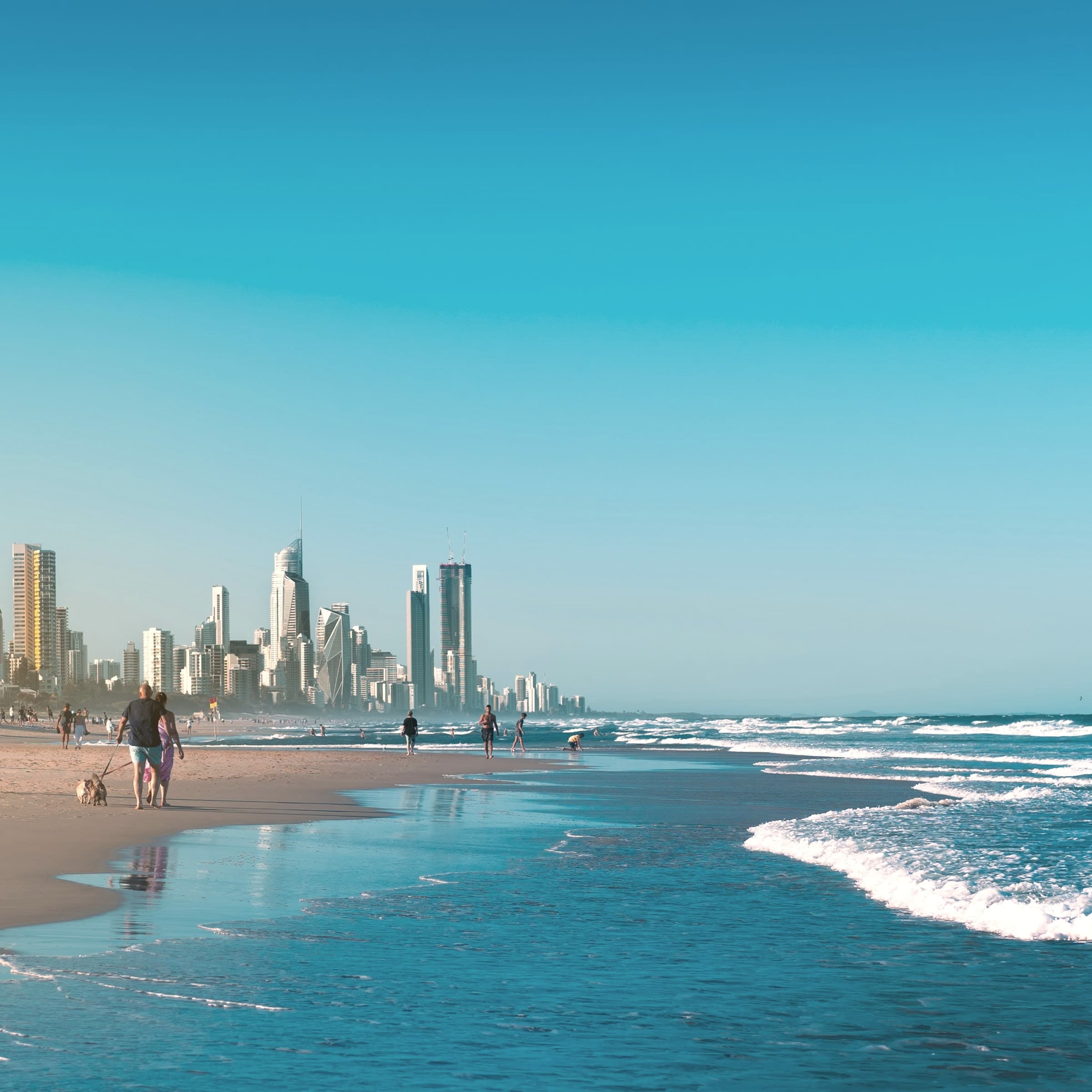 People walking along a Gold Coast beach with waves and the skyline beyond