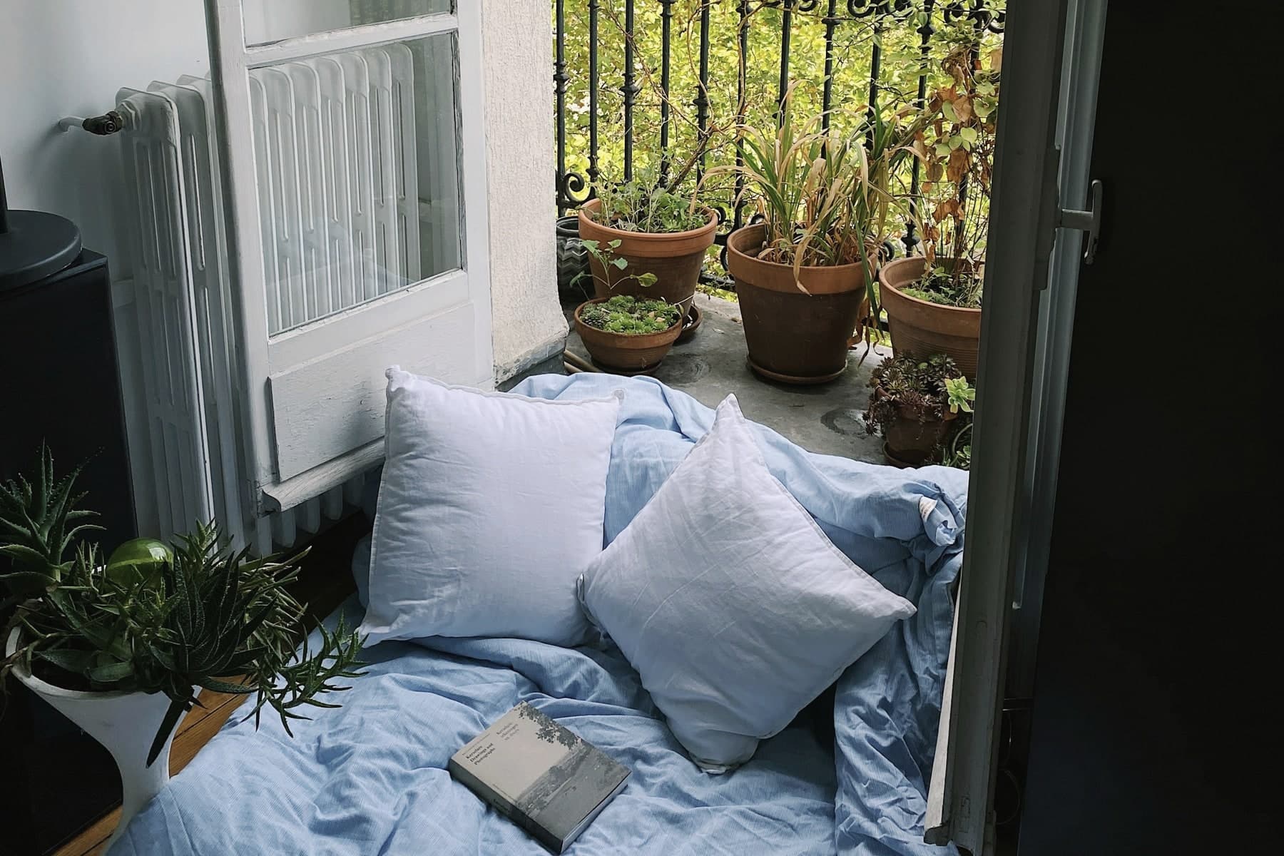 Blue bedding and a book beside open balcony doors overlooking Paris